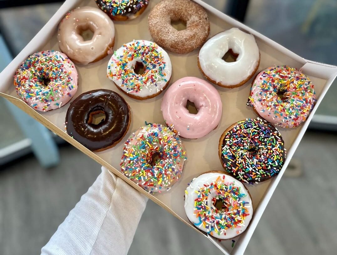 Staff serving custom donuts and desserts alongside coffee and breakfast treats at Duck Donuts.